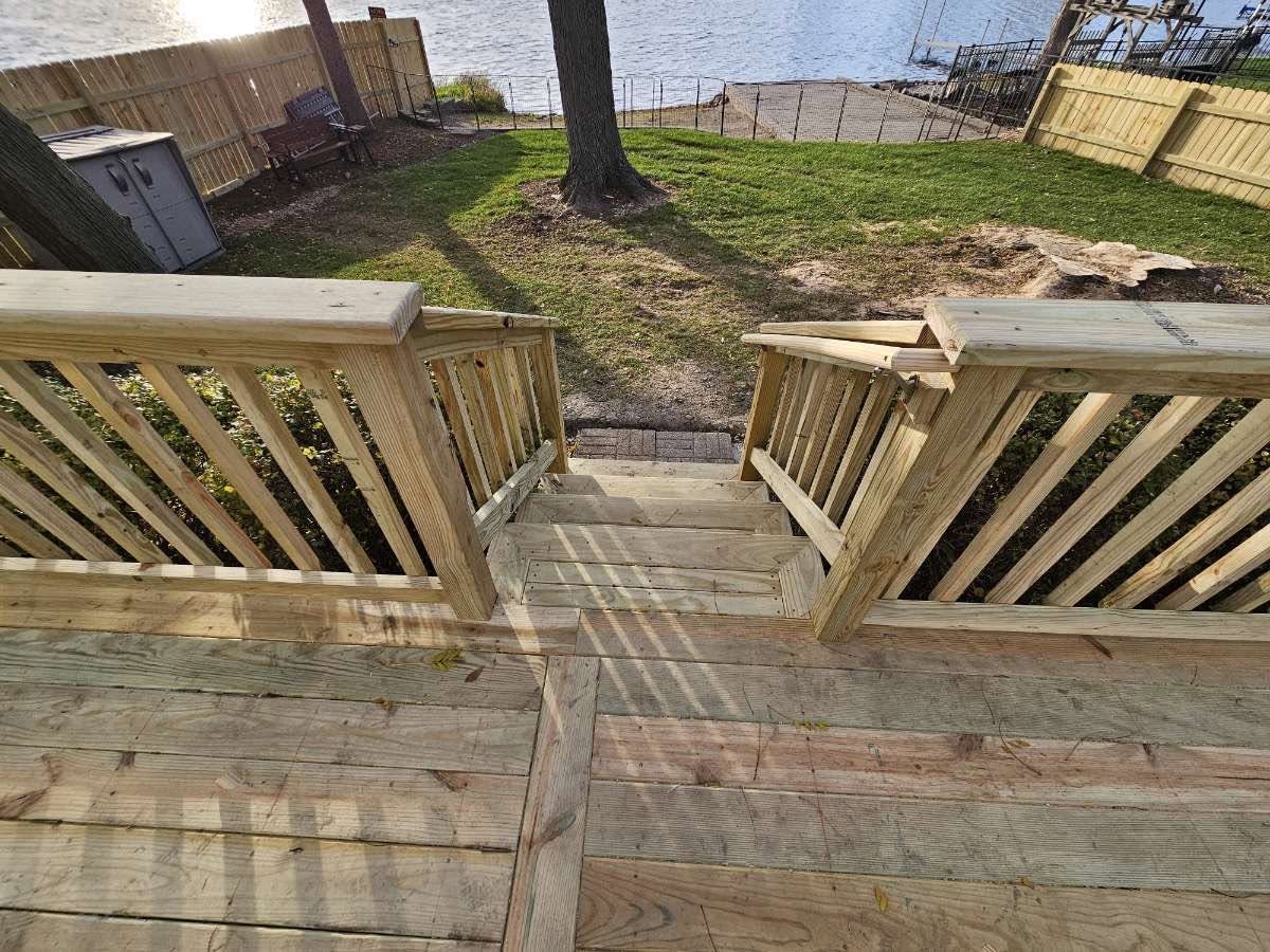 New deck stairs and railings overlooking a fenced lakefront yard