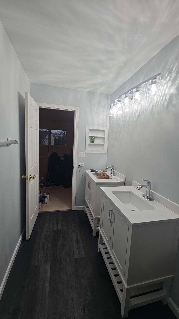 Remodeled bathroom with two white vanities and dark vinyl plank flooring