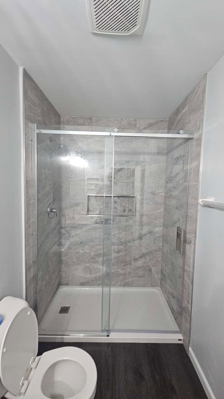Finished walk-in shower with stone-look tile and glass sliding doors