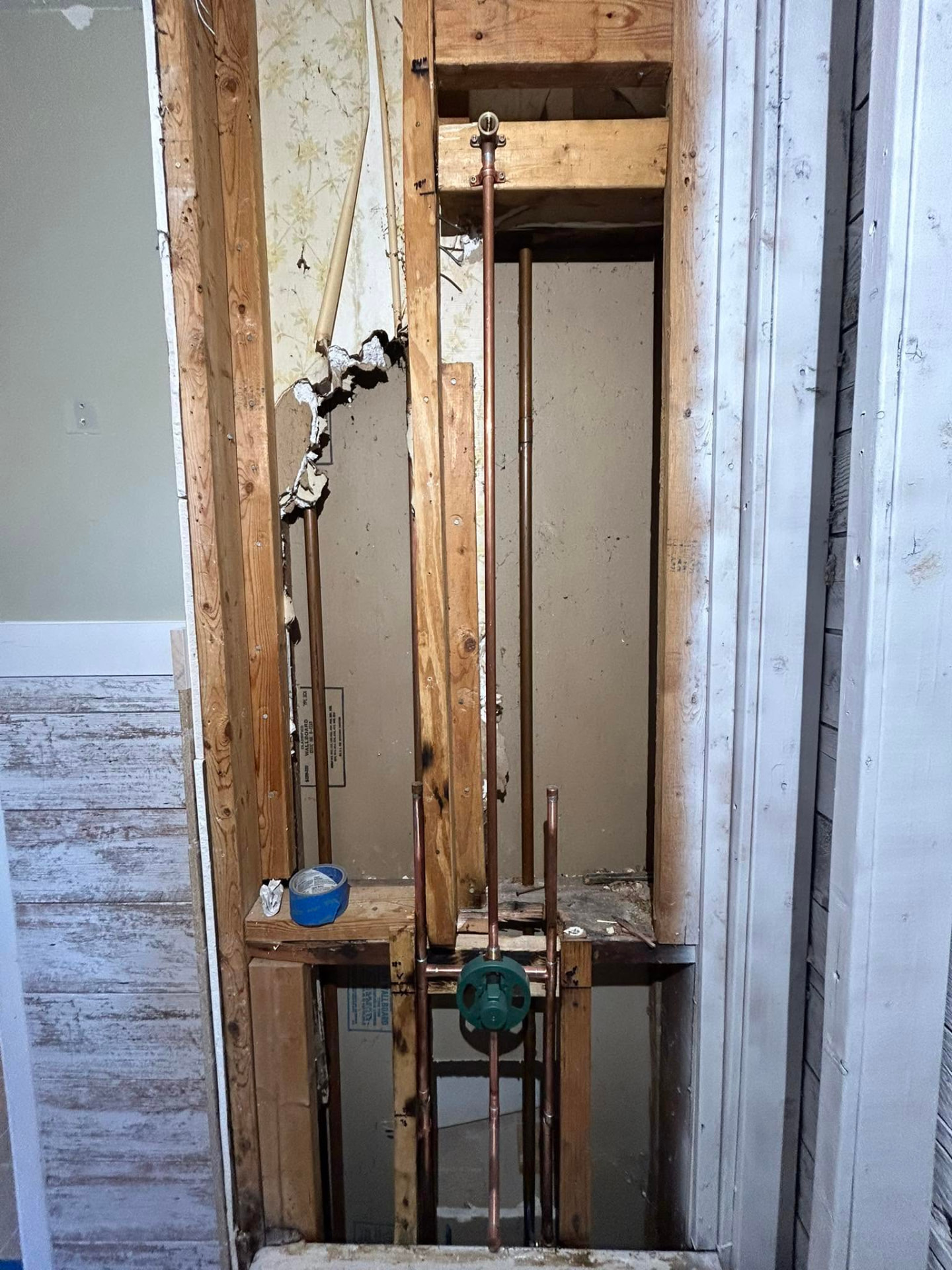 Old copper supply lines and shutoff valve exposed inside an open wall